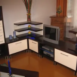 Zestaw mebli na wymiar w salonie: ciemnobrązowe korpusy z białymi frontami, srebrne uchwyty, narożne półki z podświetleniem, telewizor i sprzęt RTV, dekoracje i oświetlenie w tle.